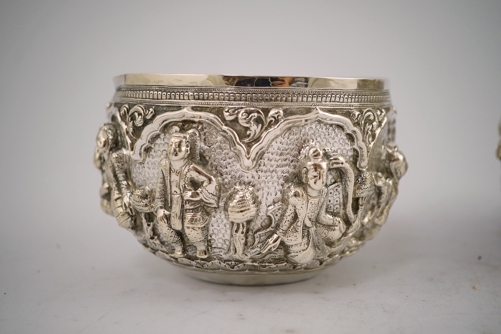 A pair of Burmese white metal bowls, embossed with figures, 12cm diameter, 220 and 224g and a plainer bowl, 110g. Condition – fair